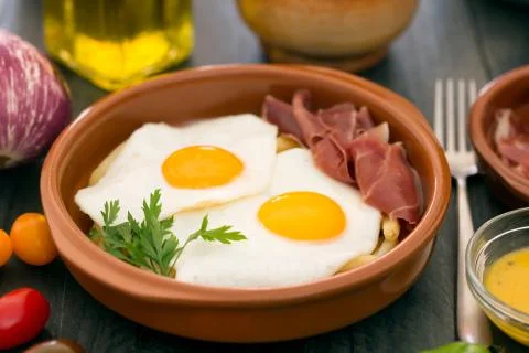 Fried eggs in a ceramic cup with spanish jamon for breakfast on a dark wooden Fotos de archivo