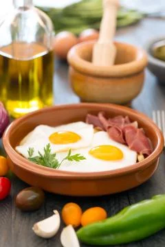 Fried eggs in a ceramic cup with spanish jamon for breakfast on black backgro Stock Photos