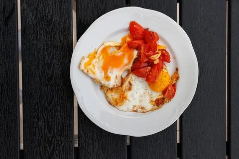 Fried eggs with cherry tomatoes served on white plate placed on a dark wood.. Stock Photos