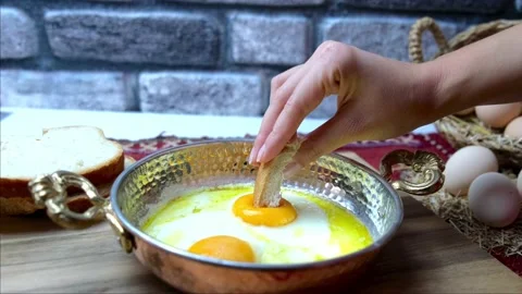 Fried eggs in a copper pan for breakfast, a woman dips bread into an egg. Stock Footage 145120495