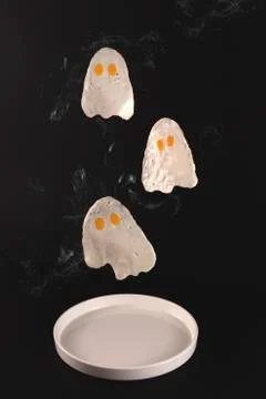Fried eggs in the form of ghosts fly over a white plate on a black background Foto stock