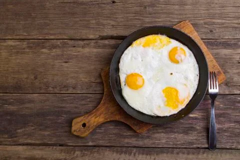 Fried eggs four eggs in a pan and fork on a cutting board on the boards Foto stock