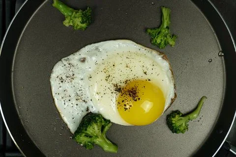 Fried eggs in a frying pan sprinkled with spices and salt with broccoli Stock Photos