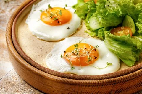 Fried eggs with micro greens, lettuce and cherry tomatoes on beige backgrou.. Stock Photos