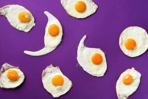 Fried eggs or scrambled eggs pattern on violet background. Creative food concept Stock Photos