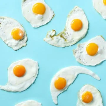 Fried eggs or scrambled eggs pattern on blue background. Creative food concept Stock Photos