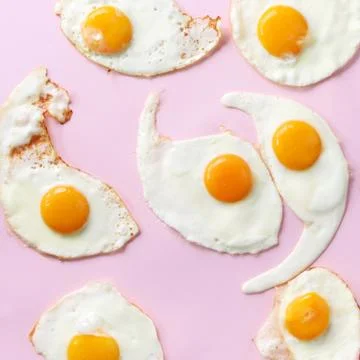 Fried eggs or scrambled eggs pattern on pink background. Creative food concept Stock Photos