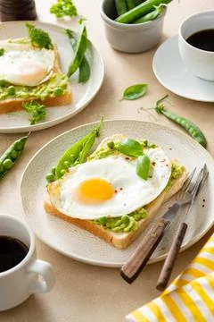 Fried eggs over bread toast with mashed avocado, coffee cups. Healthy breakfa Stock Photos