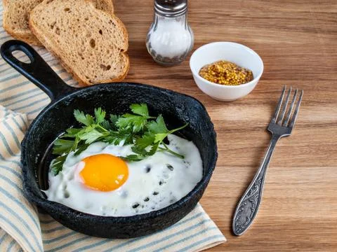 Fried eggs in a pan, bread, salt, fork on wooden background Stock Photos