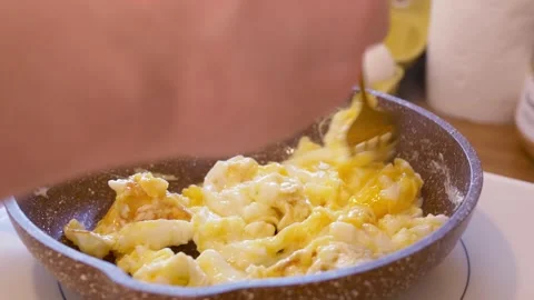 Fried eggs in a pan stirred with fork for hearty meal before hard day's work Stock Footage 220208681