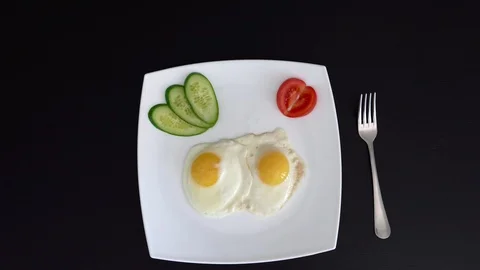 Fried eggs on a plate with vegetables. A look with top. A white plate on a black Stock Footage 88300721