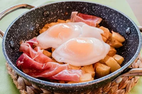 Fried eggs with potatoes and ham in a pan. Typical Spanish tapa Stock Photos