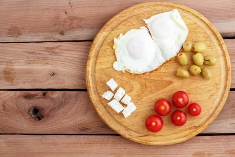 Fried eggs, scrambled eggs, cheese, olives and tomatoes on wooden tray on woo Stock Photos