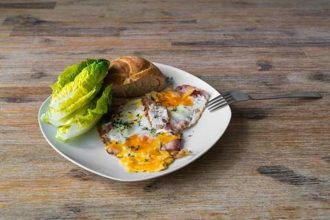 Fried eggs served with bread roll and fresh lettuce on white plate placed o.. Fotos de archivo