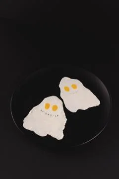 Fried eggs in the shape of halloween ghosts on black background Stock Photos