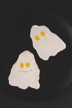 Fried eggs in the shape of halloween ghosts on black background Stock Photos