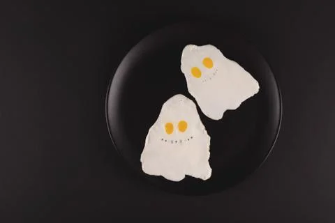 Fried eggs in the shape of halloween ghosts on black background Stock Photos