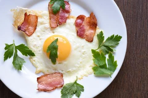 Fried eggs with slightly fried bacon and parsley on a white plate. Stock Photos