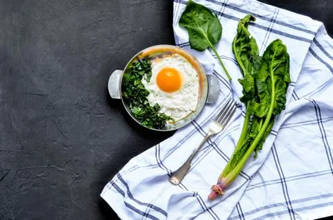 Fried eggs with spinach on iron pan plate. Fried eggs breakfast on dark black Stock Photos