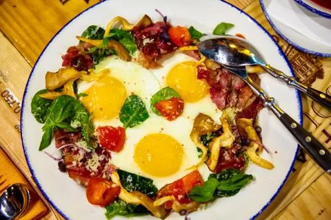 Fried eggs from three eggs with tomatoes, bacon and greens Stock Photos