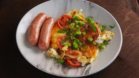 Fried eggs with tomatoes and fried sausages sprinkled with green onions on .. 库存影片 282736356
