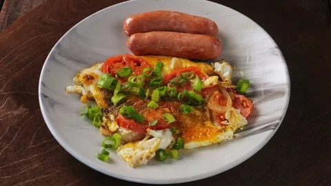 Fried eggs with tomatoes and fried sausages sprinkled with green onions on a Video stock 288739136