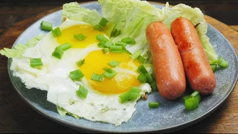 Fried eggs of two eggs with sausages sprinkled with green onions on a plate on a Stock Footage 276505667