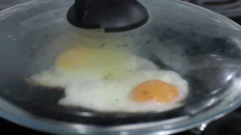 Fried eggs under a lid in a frying pan, the cook closes the frying pan with a Stock Footage 166644887