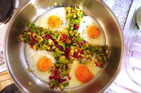 Fried eggs with vegetables in pan Stock Photos