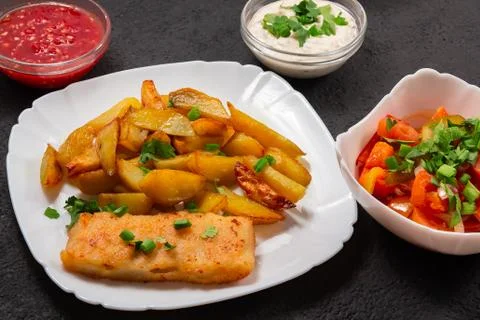 Fried fish and chips on a white plate on the black kitchen table with tomato  Stock Photos