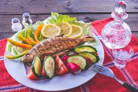 Fried fish dish with vegetables and vodka on a tablecloth Stock Photos