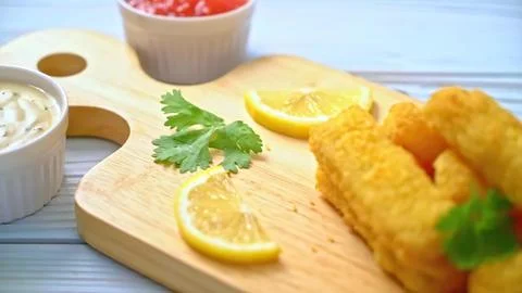 Fried fish fillets with lemon slices and sauces on a wooden board Stock Photos