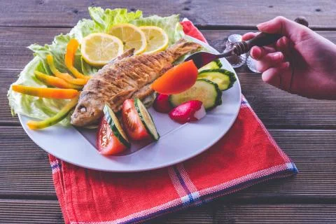 Fried fish with fresh vegetables on the tablecloth, fried in nature Stock Photos