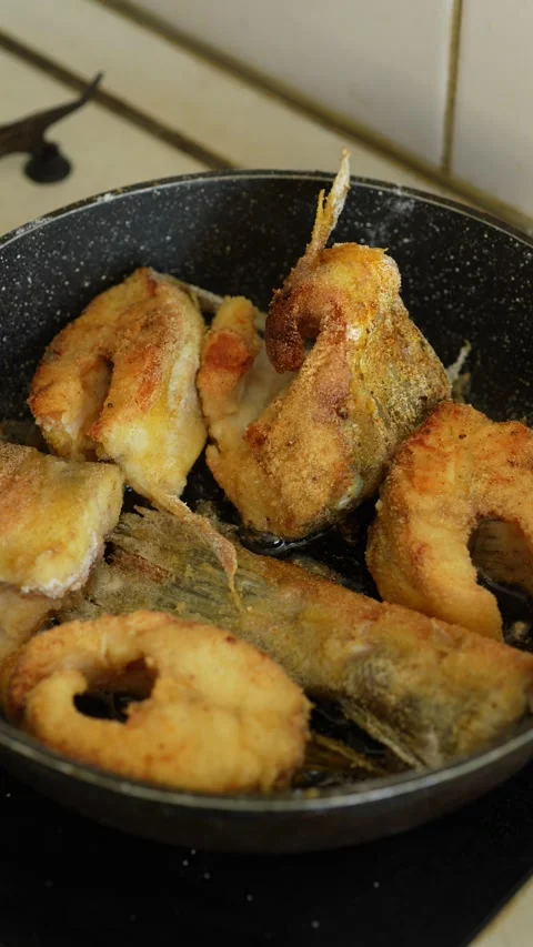 Fried fish steaks and a tail portion cooking in a black frying pan. Stock Footage 344784066