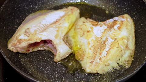 Fried flounder in a heated pan in boiling oil. The cook pours oil on the pan. Video stock 267899487