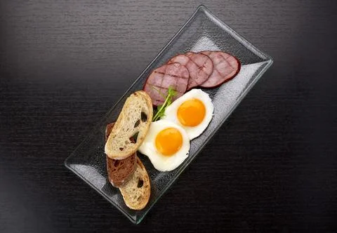 Fried fried eggs with tomatoes, ham and ciabatta toast, on a dark background. Foto stock