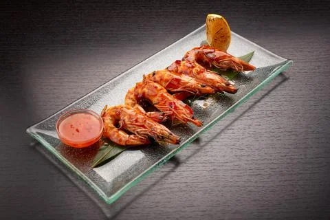 Fried king prawns on a bamboo leaf, on a transparent plate, with lemon and sa Stock Photos