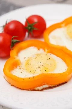Fried organic eggs inside orange paprika rings. Eggs with tomatoes and paprik Stock Photos
