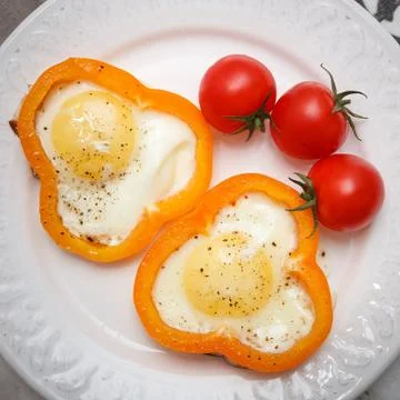 Fried organic eggs inside orange paprika rings. Eggs with tomatoes and paprik Stock Photos