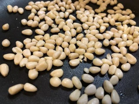 Fried pine nuts on black frying pan Stock Photos