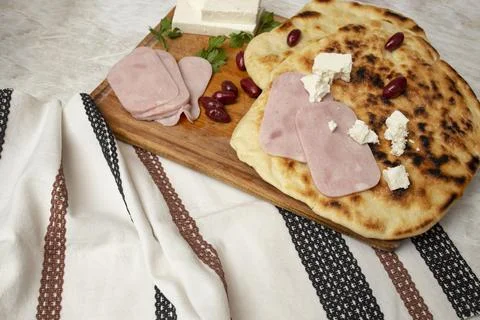 Fried pita bread stack on a wooden chopping board with ham slices and goat .. Stock Photos