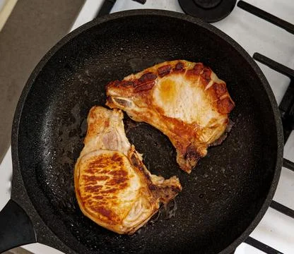 Fried pork steaks with a bone lie in a frying pan. Stock Photos