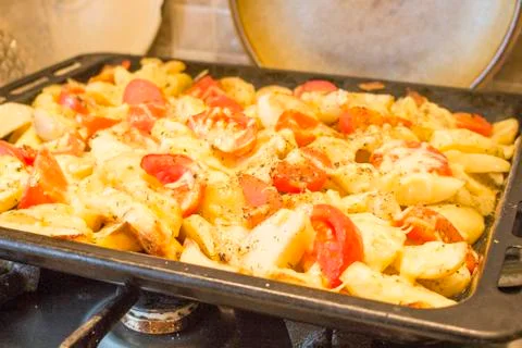 Fried potatoes with red tomatoes on a baking sheet Stock Photos
