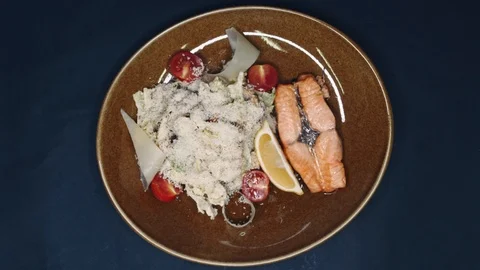 Fried red fish and lettuce sprinkled with parmesan with a slice of lemon in a Stock Footage 99223686