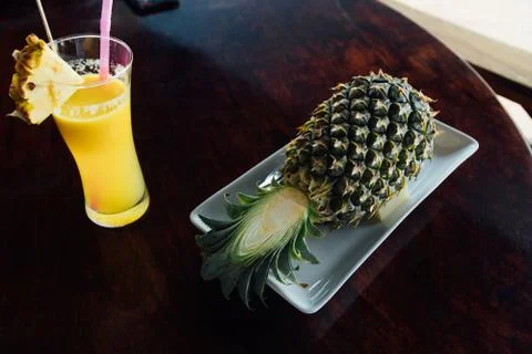 Fried rice inside pineapple next to a glass of juice with a straw and slices of Stock-Fotos
