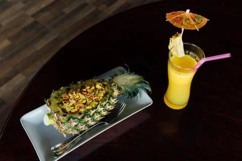 Fried rice inside pineapple next to a glass of juice with a straw and slices of Stock Photos