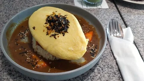 Fried rice topped with fluffy omelet and savory sauce, served on a plate. Stock Footage 336608918