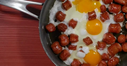 Fried sausages with chicken eggs in process of frying in a frying pan Stock Footage 142706330