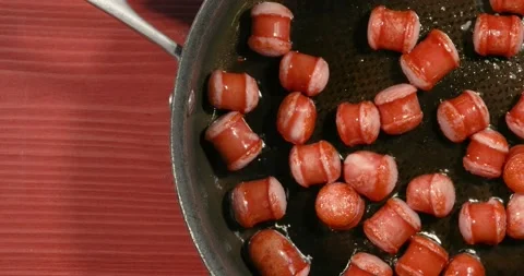 Fried sausages in process of frying in a frying pan at the red wood table Stock Footage 142706332