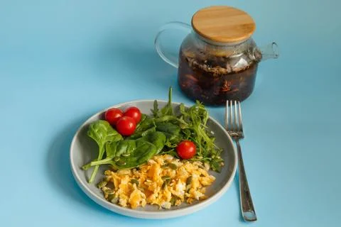 Fried scrambled eggs with spinach and tomatoes with tea on blue background Stock Photos